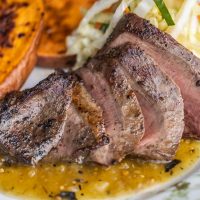 sliced grilled lamb heart with salsa verde sweet potatoes and cabbage slaw