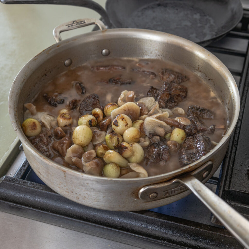 goat neck pieces in a pan with mushrooms and onions