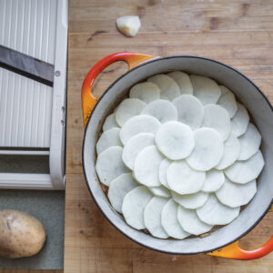 covering stew with sliced potatoes in a dutch oven